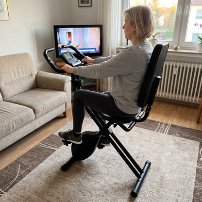 Frau trainiert auf dem VeloFold Pro im Wohnzimmer vor dem Fernseher