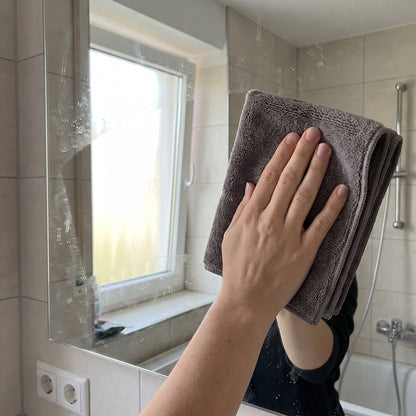 Hand poliert einen Badezimmerspiegel mit einem grauen Mikrofasertuch