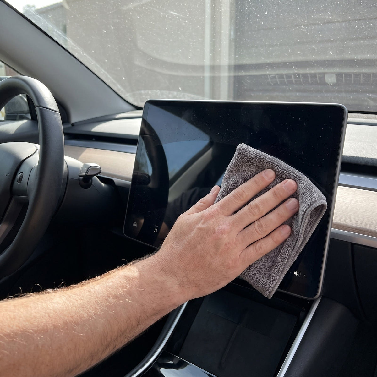Hand reinigt das Touchdisplay im Auto mit einem grauen Mikrofasertuch