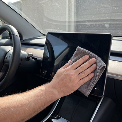Hand reinigt das Touchdisplay im Auto mit einem grauen Mikrofasertuch